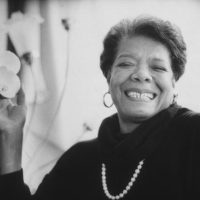 8th January 1993:  Headshot portrait of African-American author Maya Angelou wearing black sweater with a pearl necklace, smiling and holding flowers in one hand.  (Photo by Stephen Matteson Jr/New York Times Co./Getty Images)